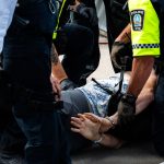 Policiais detêm uma pessoa algemada em uma rua durante uma operação.