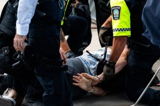 Policiais detêm uma pessoa algemada em uma rua durante uma operação.