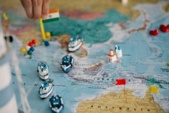 Mapa-múndi com pequenos navios e bandeiras indicando diferentes localidades e rotas comerciais globais.
