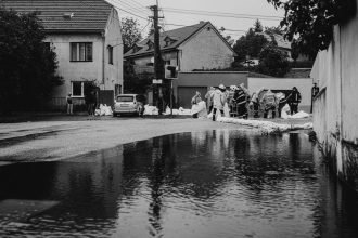 Profissionais com capas de chuva constroem barreiras de sacos de areia durante uma inundação urbana.