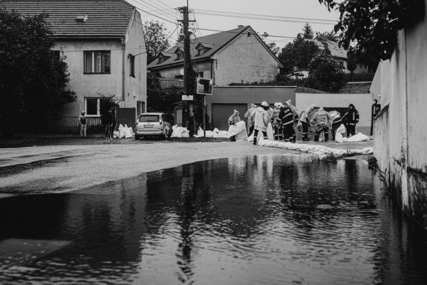 Profissionais com capas de chuva constroem barreiras de sacos de areia durante uma inundação urbana.