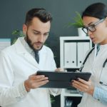 Dois médicos analisam informações de saúde em um tablet em ambiente clínico.