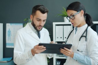 Dois médicos analisam informações de saúde em um tablet em ambiente clínico.