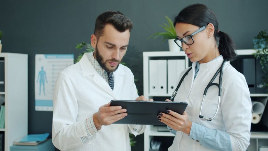 Dois médicos analisam informações de saúde em um tablet em ambiente clínico.